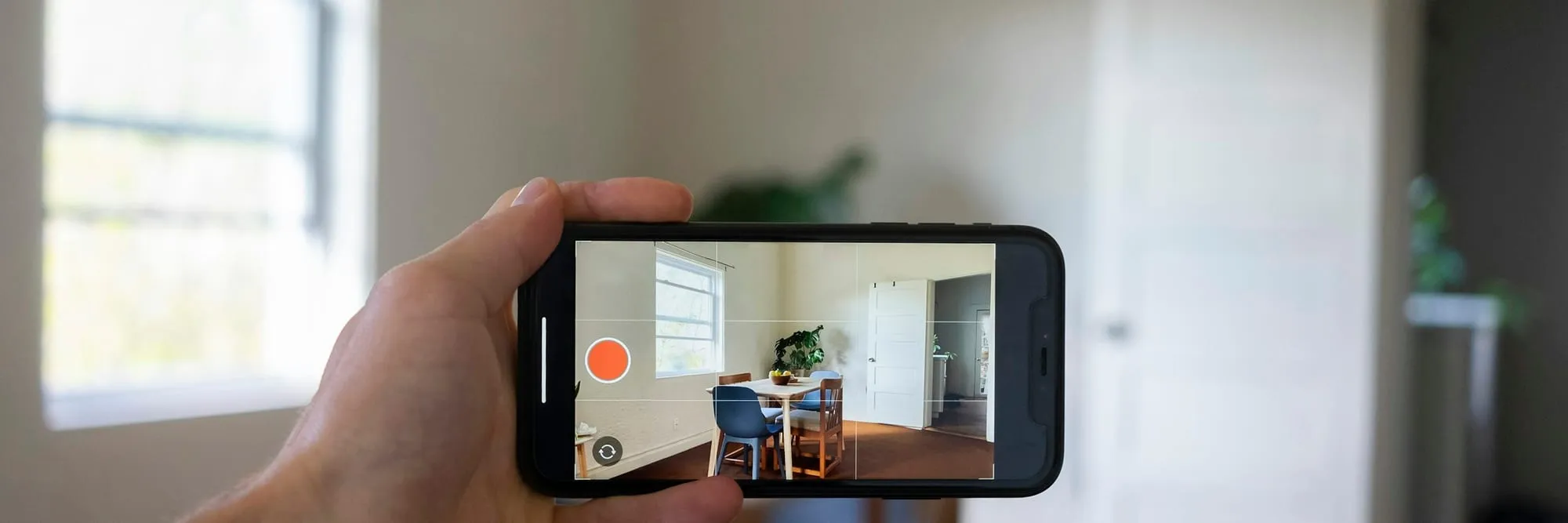 A hand holding a phone up to record a plain, empty furnished room during a property visit.